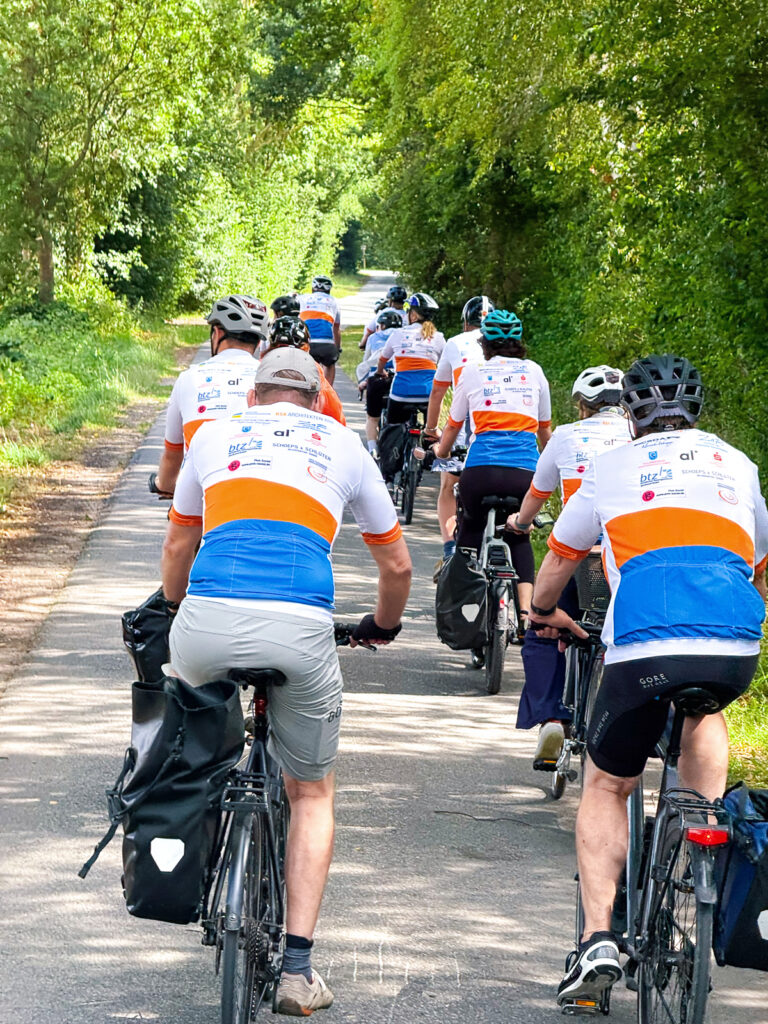 Rückansicht der Teilnehmenden der RPK-Radtour 2025 auf Landstraße im Grünen