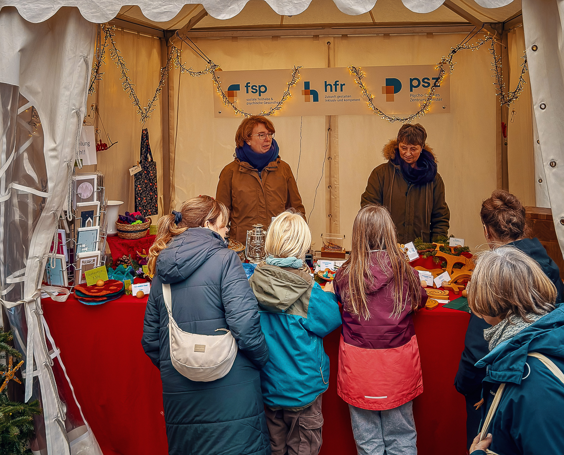 Handgemachte Produkte und Dekoartikel am FSP-Weihnachtsmarktstand mit Besucherinnen.